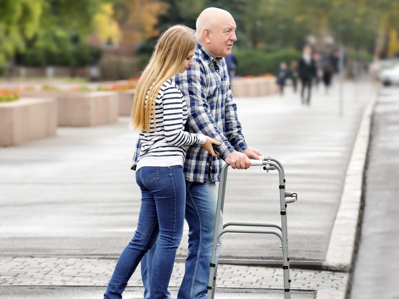 O tânără ajută un vârstnic să traverseze strada