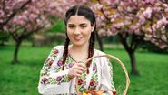Tânără îmbrăcată în costum tradițional, coș cu ouă vopsite pentru Paște
