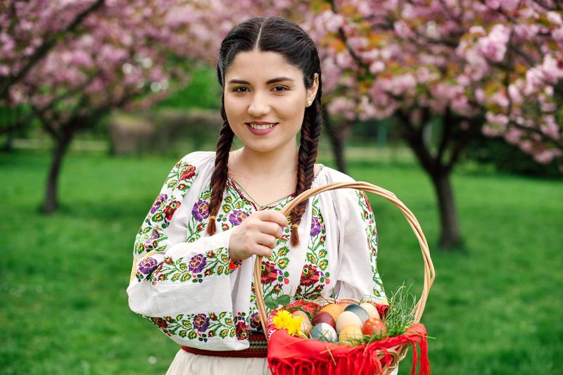 Tânără îmbrăcată în costum tradițional, coș cu ouă vopsite pentru Paște