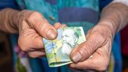 Vârstnică, ținând în mână o bancnotă de 1 leu