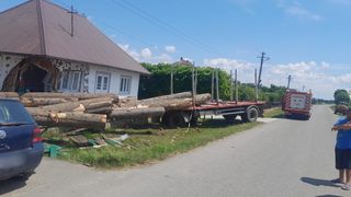 FOTO - O remorcă plină cu butuci s-a răsturnat în curțile a două case. Pompierii militari au intervenit