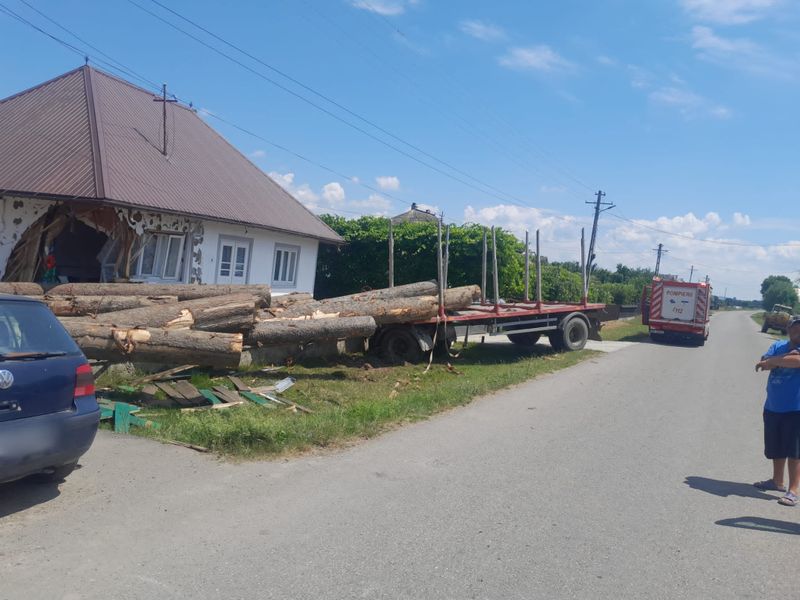 FOTO - O remorcă plină cu butuci s-a răsturnat în curțile a două case. Pompierii militari au intervenit