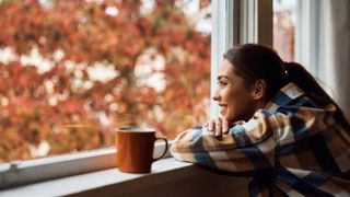 femeie fericita care priveste pe geam toamna