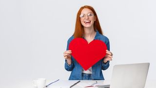 femeie care sta la birou si tine o inima in mana