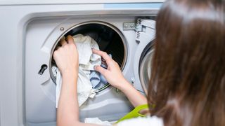 femeie care bagă rufe &icirc;n masina de spalat