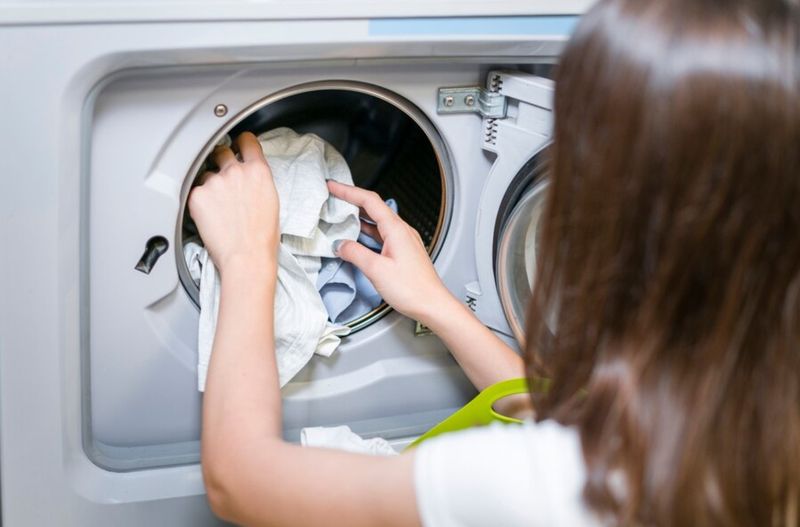 femeie care bagă rufe în masina de spalat