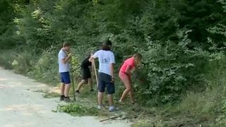 Intr-un sat din Romania, voluntari francezi strang gunoaiele. In acest timp, localnicii stau pe marginea santului si ii privesc